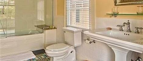 Un baño con cabina de ducha acristalada, inodoro, lavamanos y baldosas de suelo con diseño.