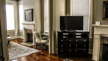 A living room with a fireplace, a television on a black entertainment unit, a white chair, and a patterned rug.