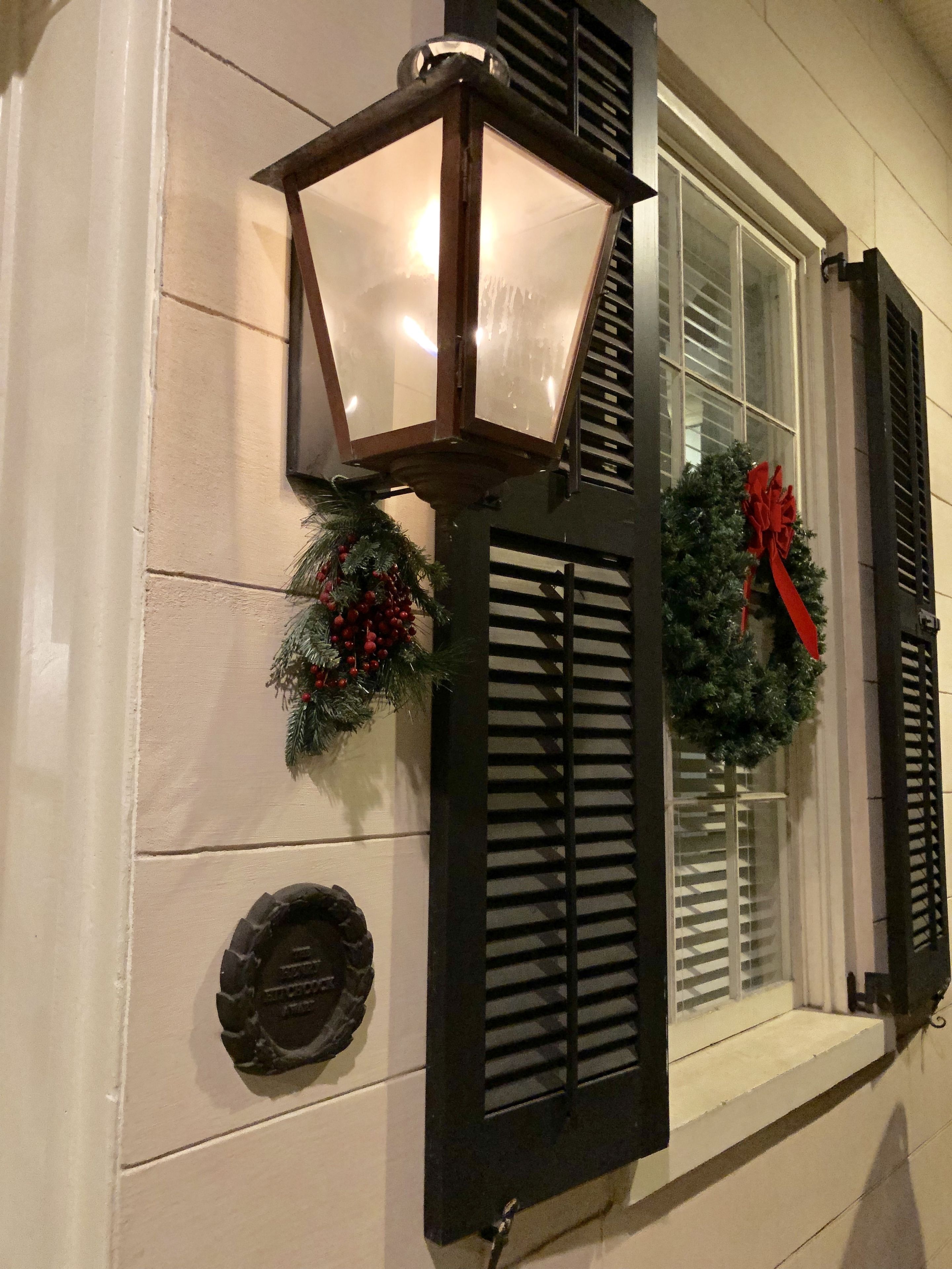 A building exterior with a decorative lantern, a wreath with a red bow, and a small plaque.