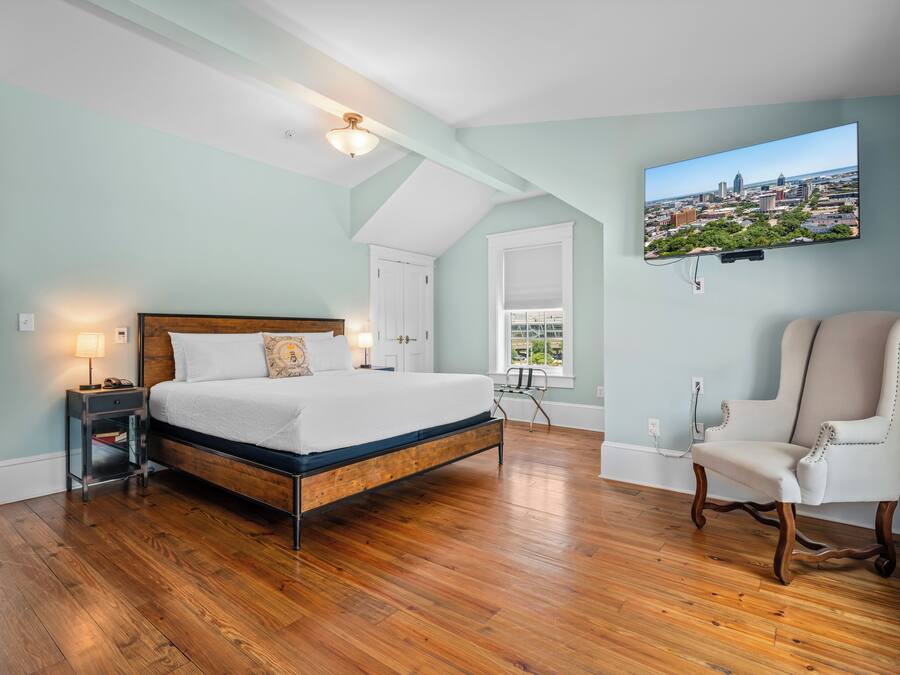 A bedroom with a large bed, a chair, a desk, and a cityscape painting on the wall.