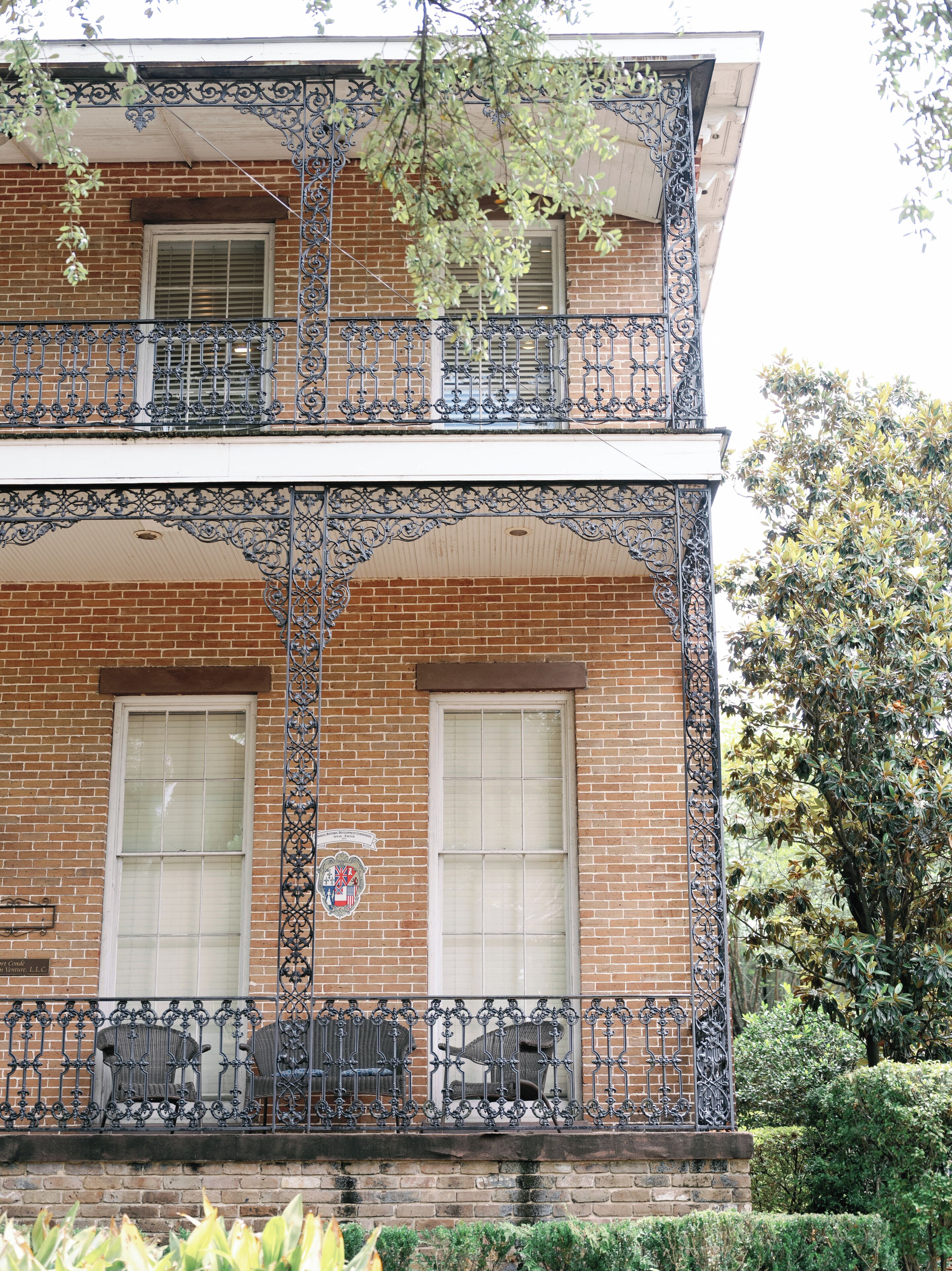 A two-story building with a brick facade, two windows on the ground floor, and a balcony with wrought iron railings.