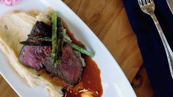 A plate of food with steak, asparagus, and sauce, a glass of red wine, and a fork and knife on a wooden table.