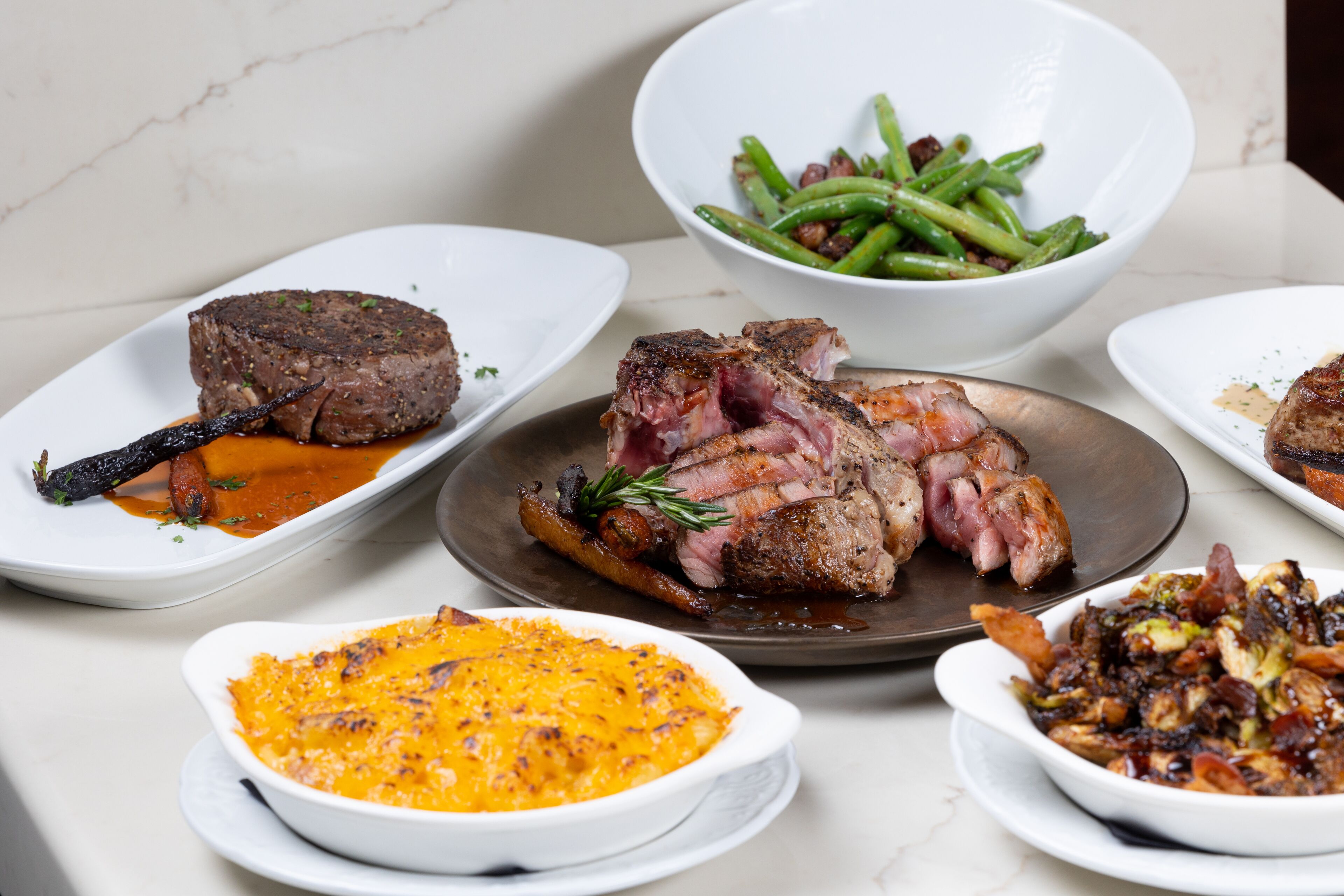 A variety of dishes including steak, green beans, and a baked dish.
