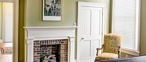 A bedroom with a fireplace, a bed, a chair, and a chandelier.