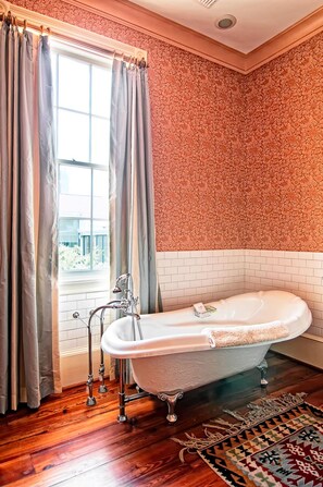 A bathroom with a freestanding bathtub, a window with curtains, and a patterned wall.
