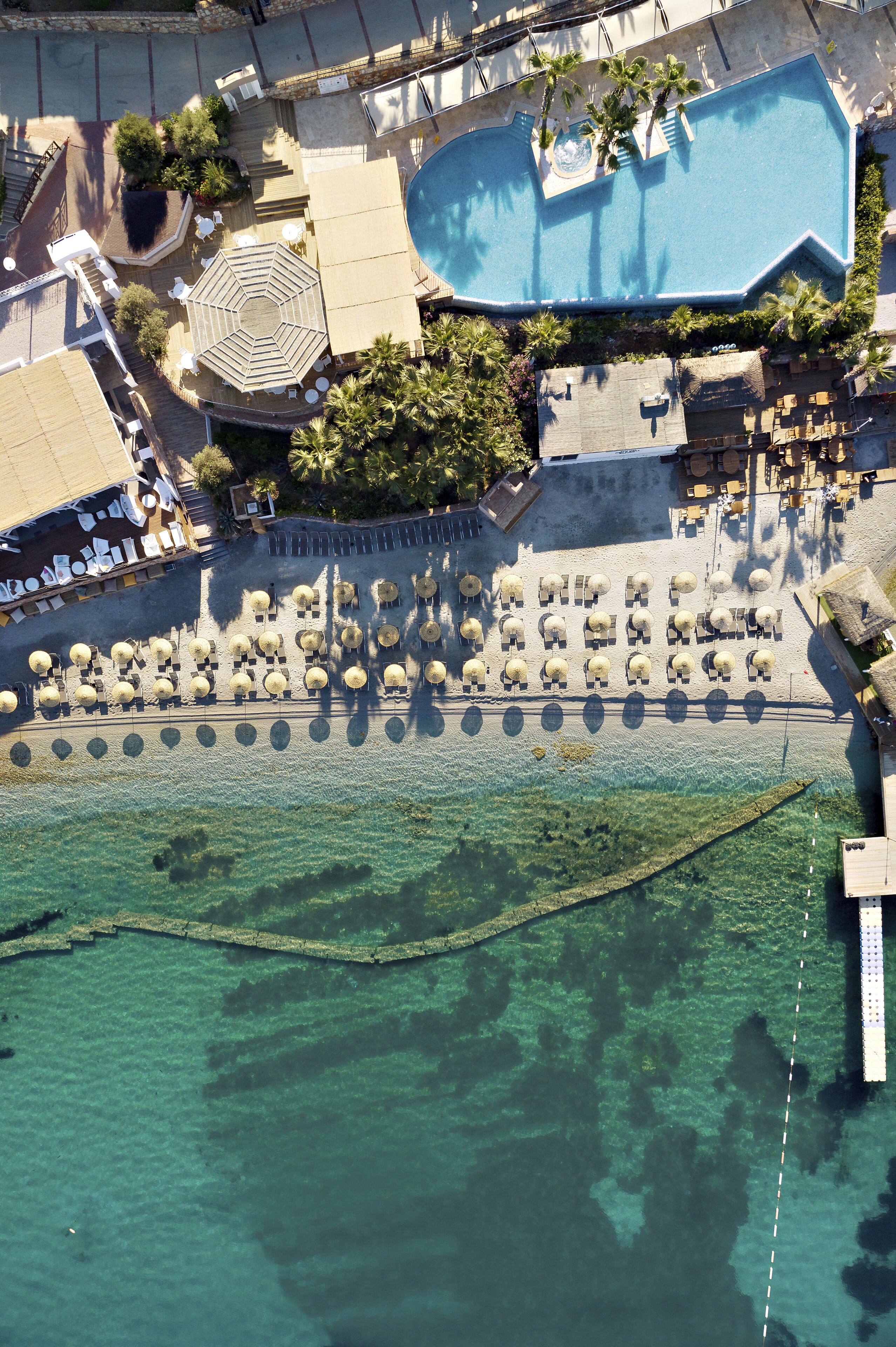 An aerial view of a resort with a swimming pool, sun loungers, and a beach area.