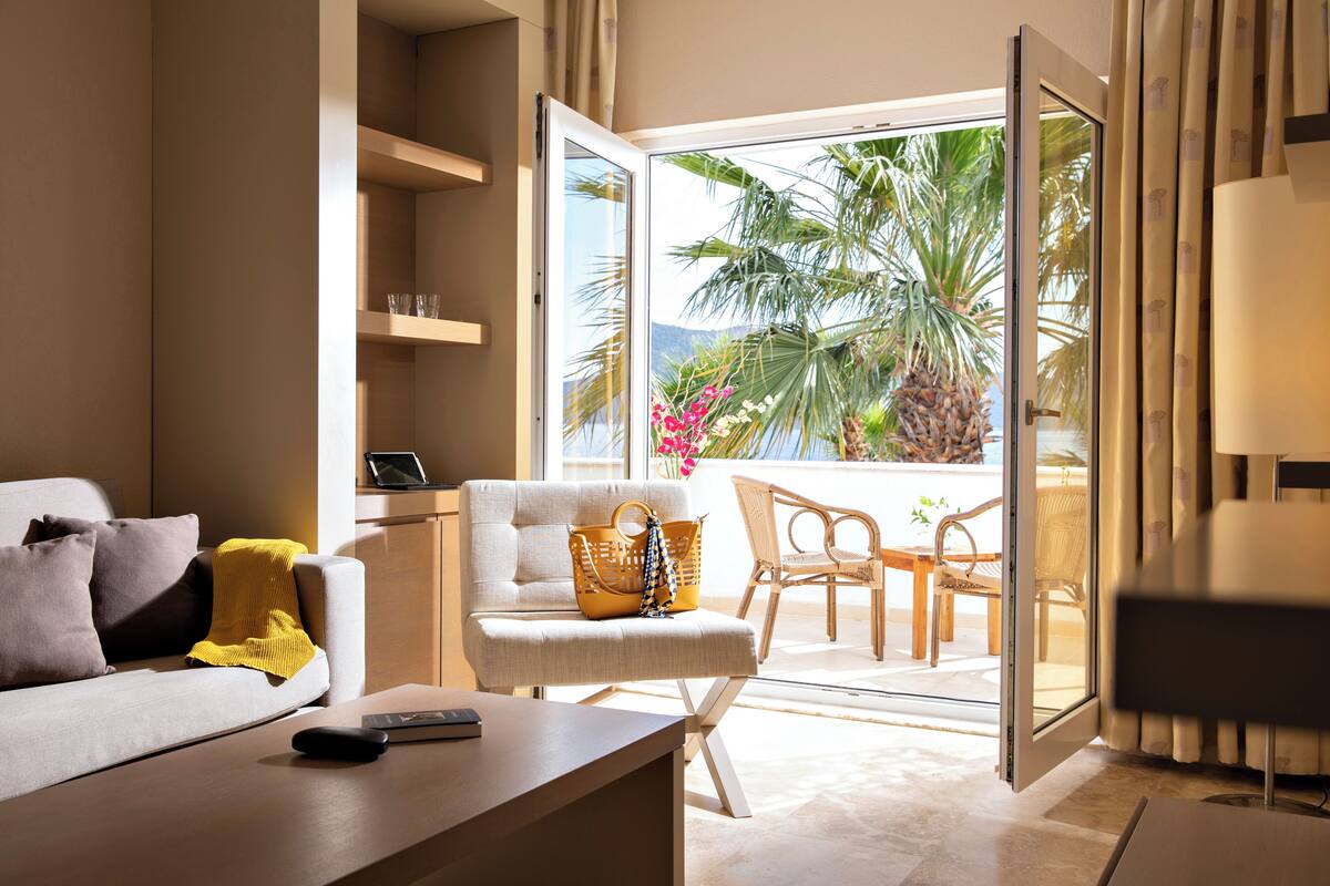Un salon moderne avec un canapé, une table basse, un fauteuil et un balcon offrant une vue sur des palmiers et des fleurs.