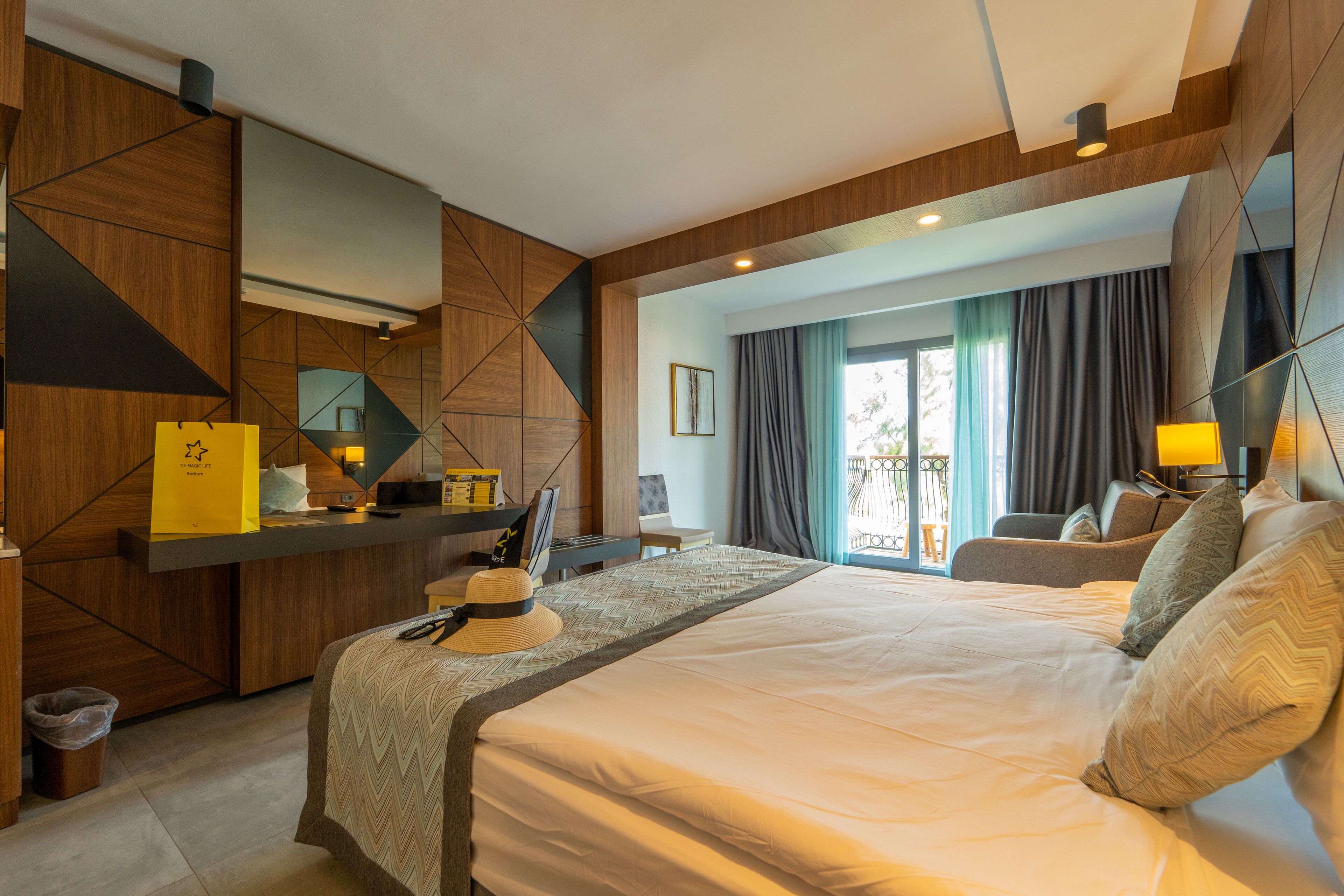 A modern hotel room with a large bed, a desk, and a view of the outdoors.