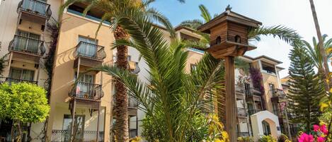 A multi-story building with balconies, palm trees, and a birdhouse.