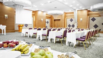 Un salón de banquetes con mesas redondas, sillas moradas y manteles blancos.