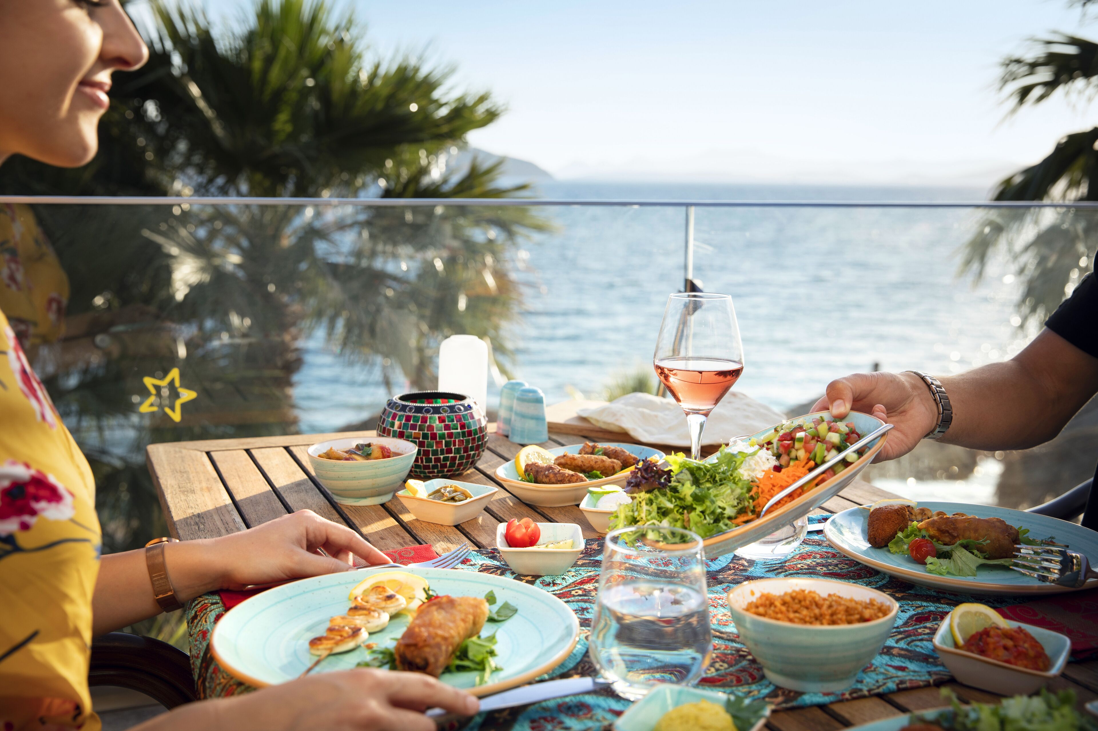 Een eettafel met diverse gerechten, een glas wijn en uitzicht op de oceaan.