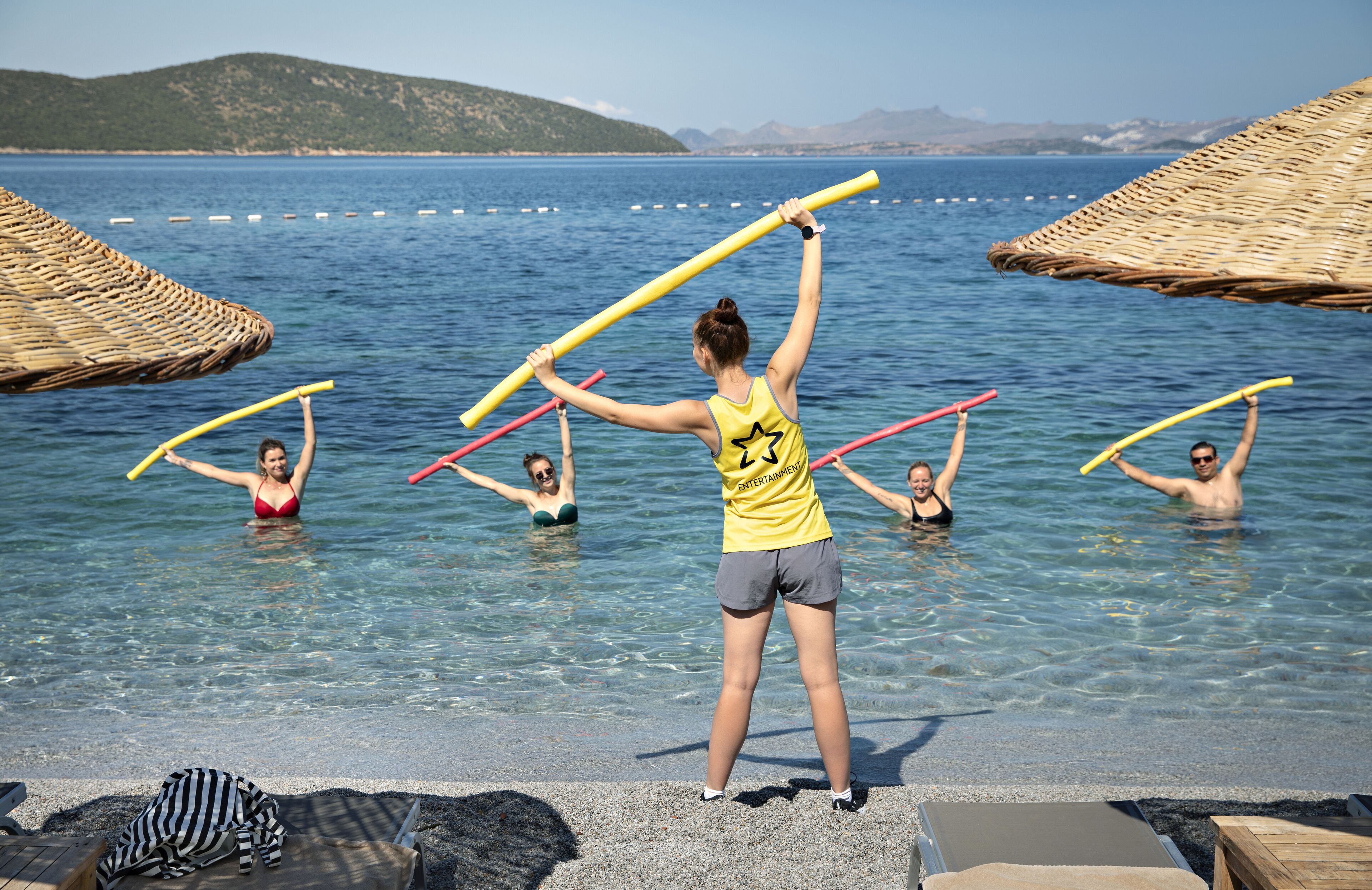 A group of people in a clear pool with a beach and umbrellas in the background.