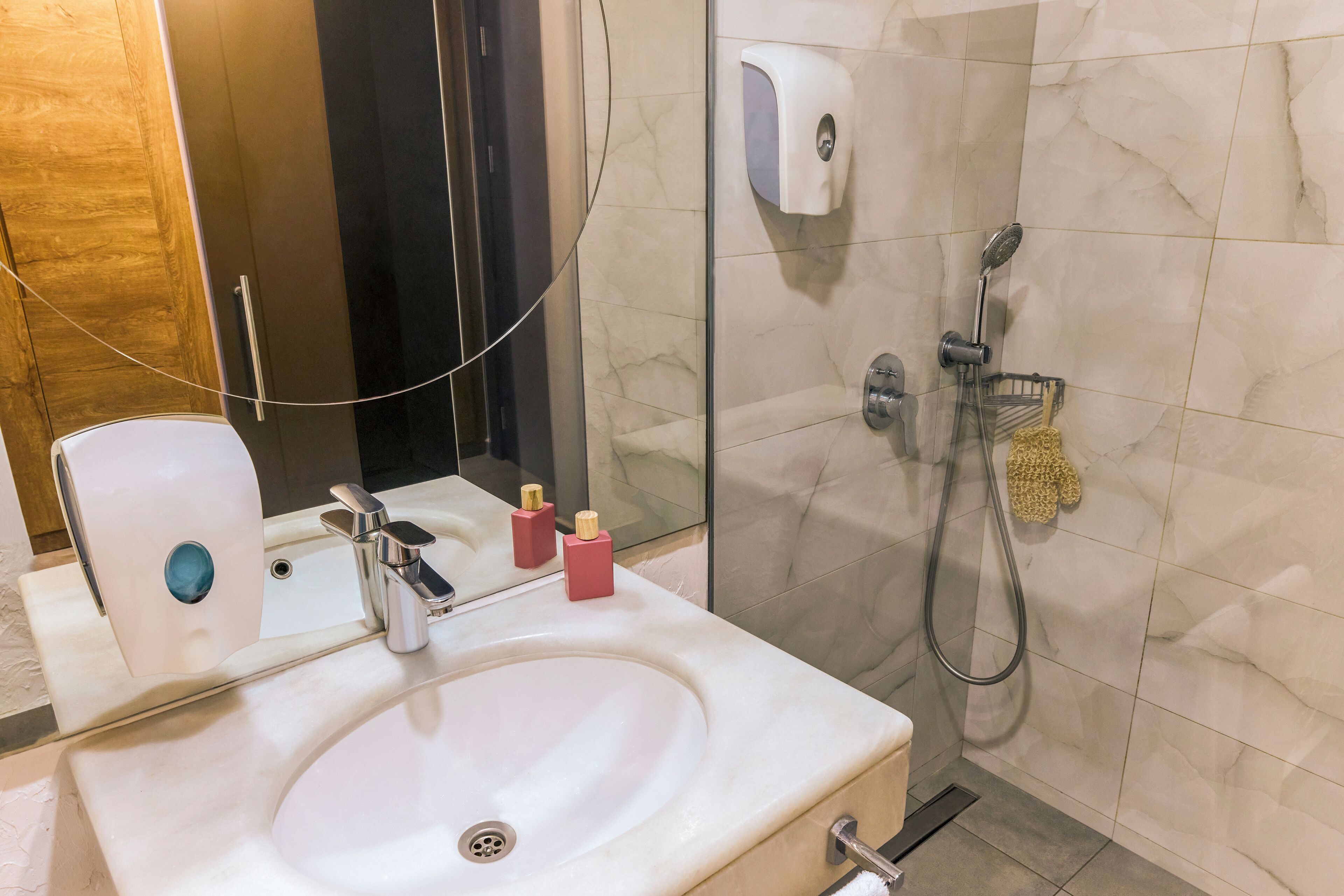 A bathroom with a white sink, a handheld showerhead, and a hand soap dispenser.