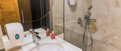Un baño con un lavamanos blanco, un cabezal de ducha de mano y un dispensador de jabón.