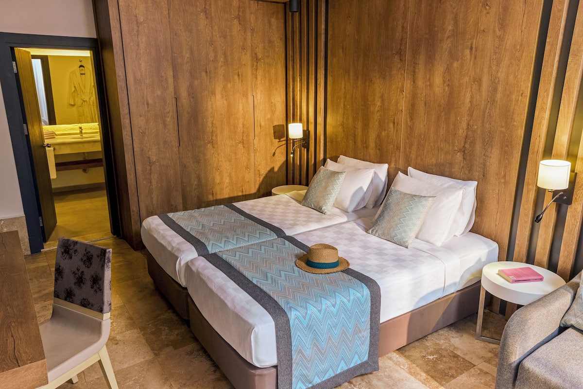Une chambre d’hôtel avec un mur en bois, un lit recouvert d’une couvre-lit à motifs, une table de chevet avec une lampe et une chaise.