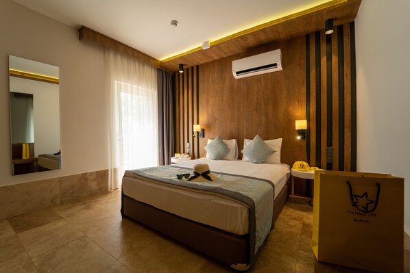 Una habitación de hotel moderna con una cama grande, una mesita de noche con lámpara, un espejo y un equipo de aire acondicionado.