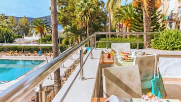 A poolside area with lounge chairs, a dining table with a meal, and a view of the pool and palm trees.