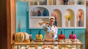 Une personne verse du thé dans une tasse sur un comptoir où sont disposées diverses pâtisseries et une citrouille décorative.