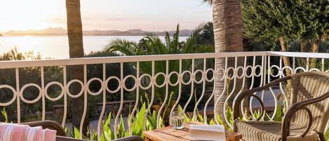 Ein Balkon mit Korbmöbeln, einem Holztisch und Blick auf das Meer und die Berge.