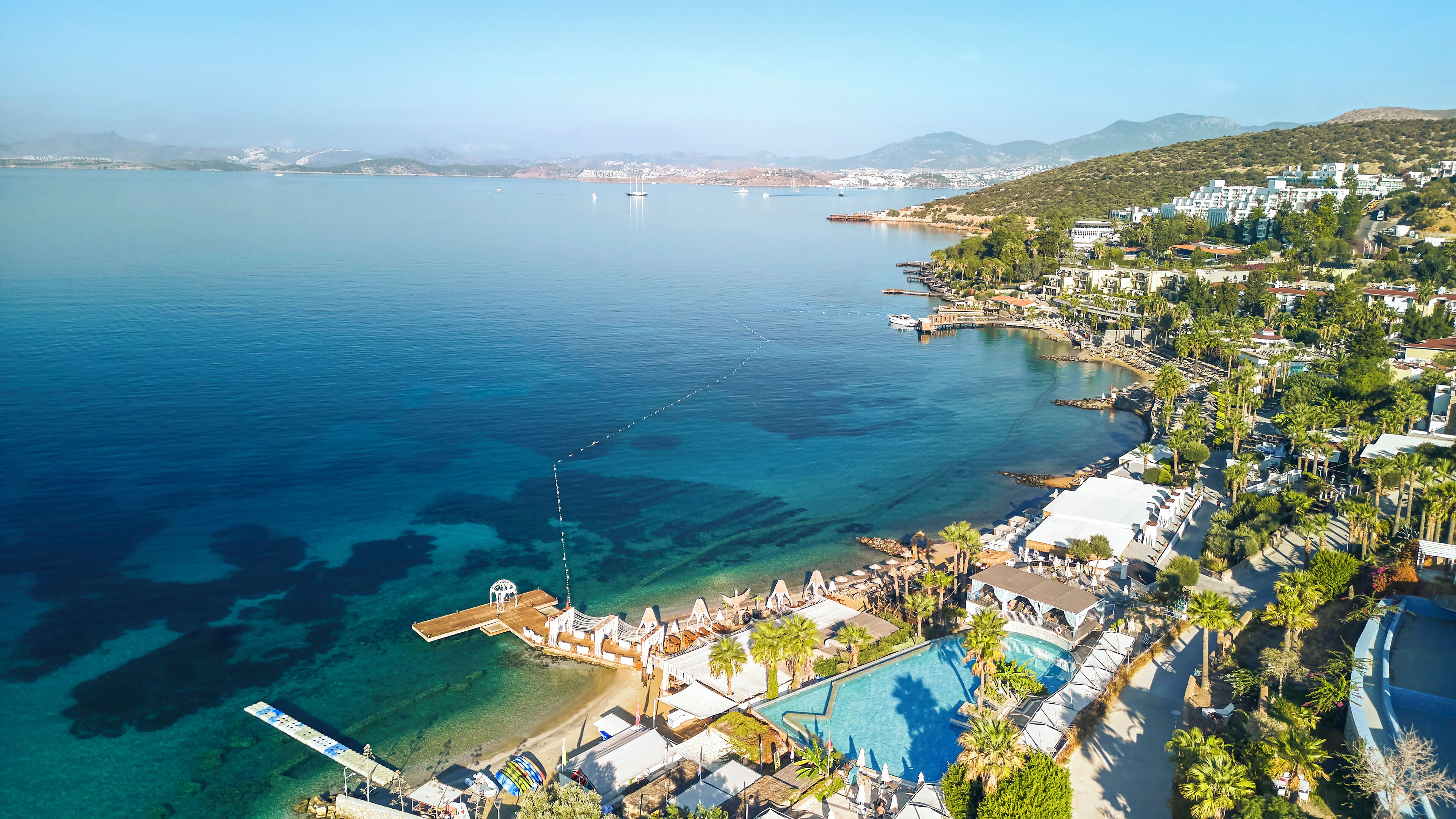 An aerial view of a coastal resort with clear waters, a beach, and a swimming pool.