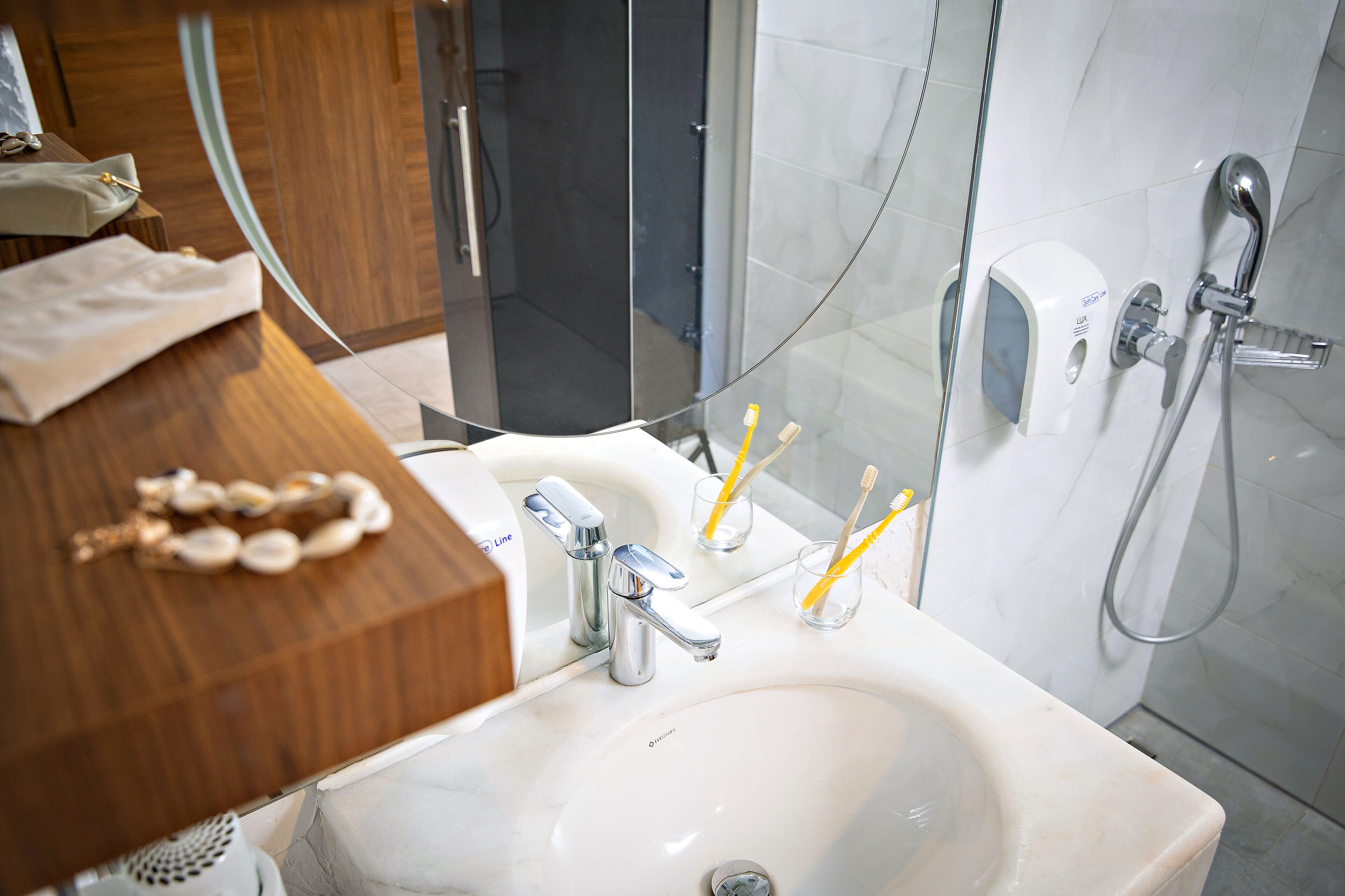 A bathroom with a white sink, two faucets, and a handheld showerhead. There are toothbrushes in a glass and a soap dispenser on the wall.