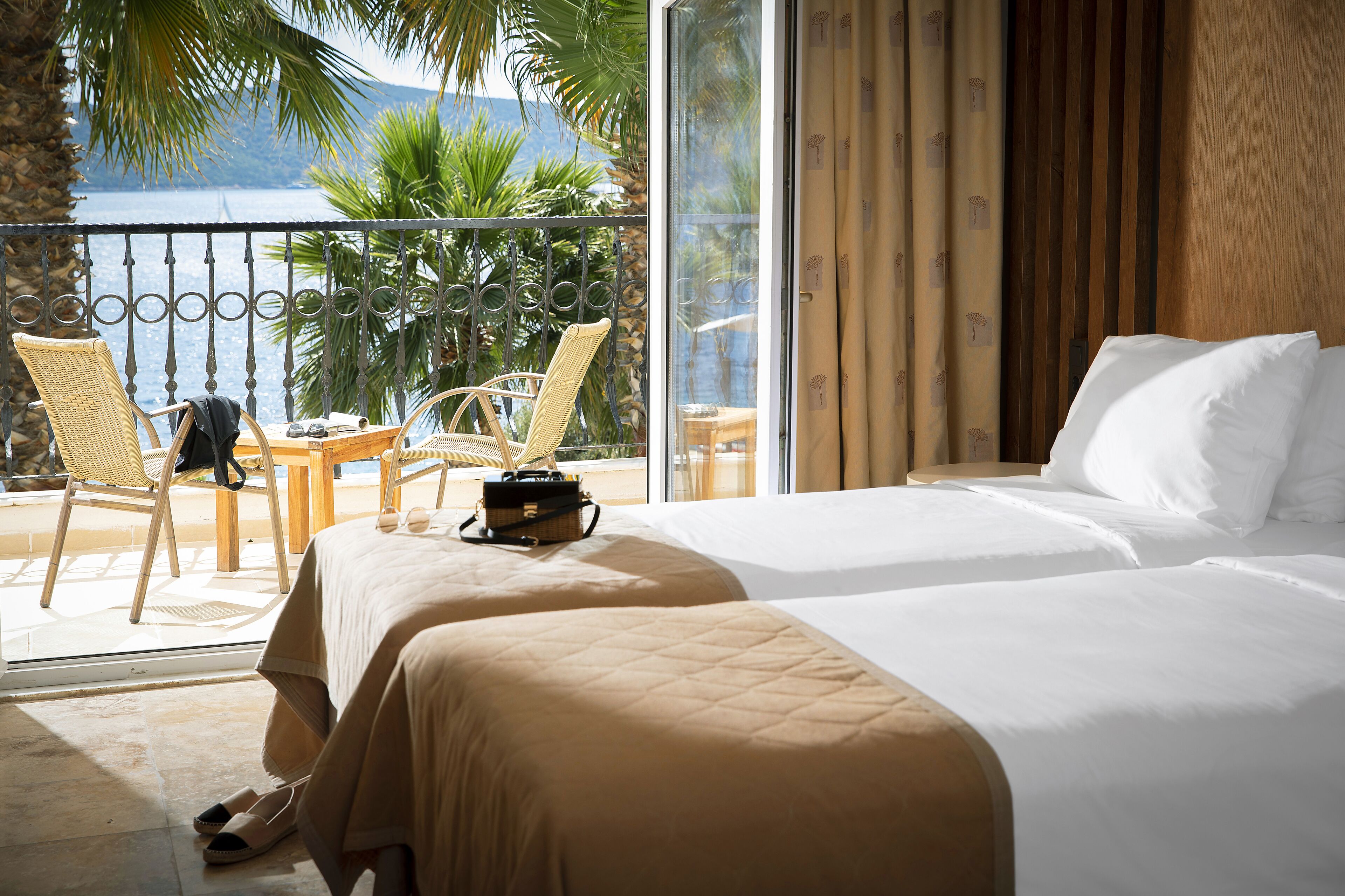 A hotel room with two beds, a balcony with a view of the sea, and a wooden wall.