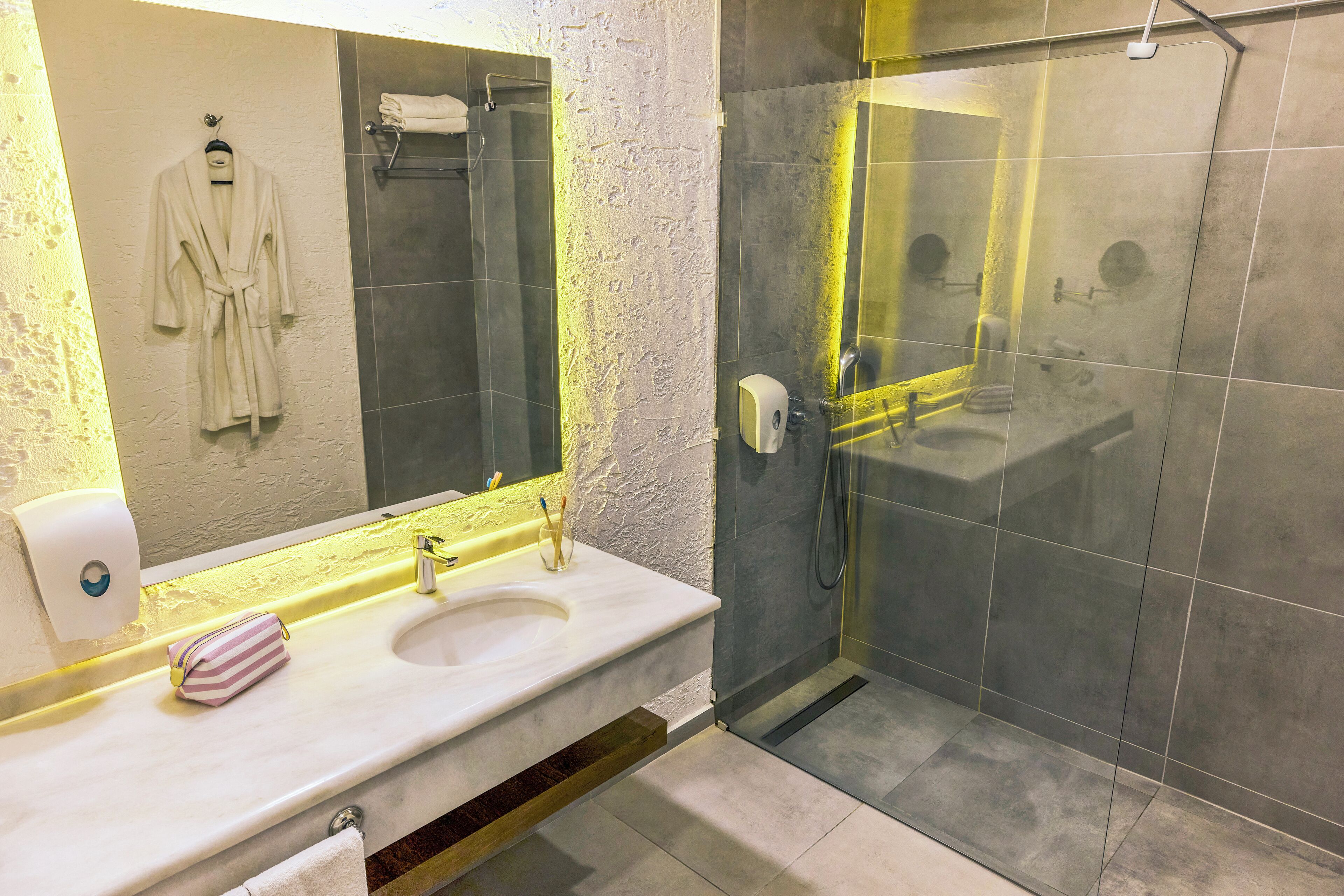 A modern bathroom with a white sink, a glass shower enclosure, and a towel rack with a robe.