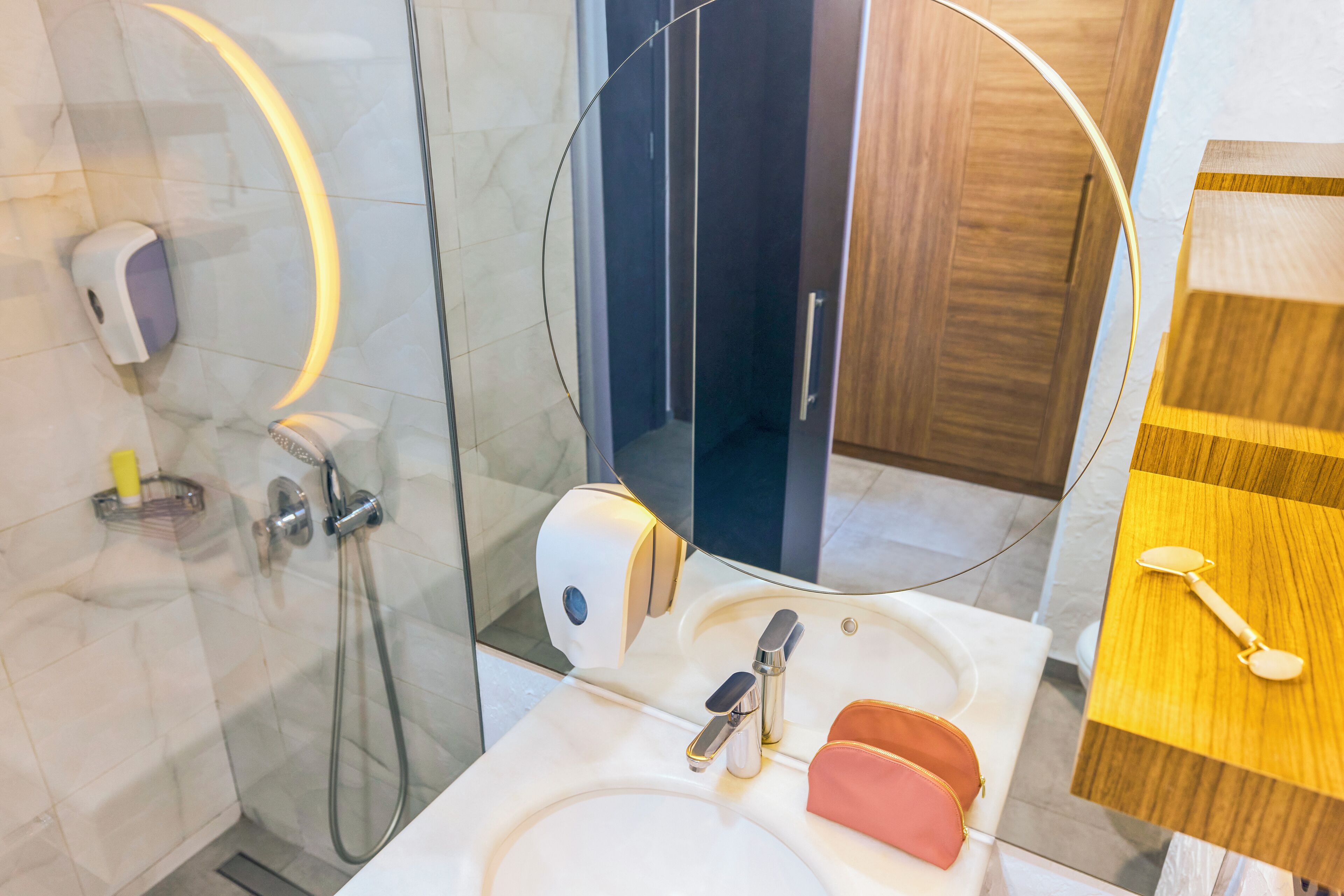 Une salle de bain moderne avec une douche à parois de verre, un lavabo blanc, un miroir et un meuble-lavabo en bois.