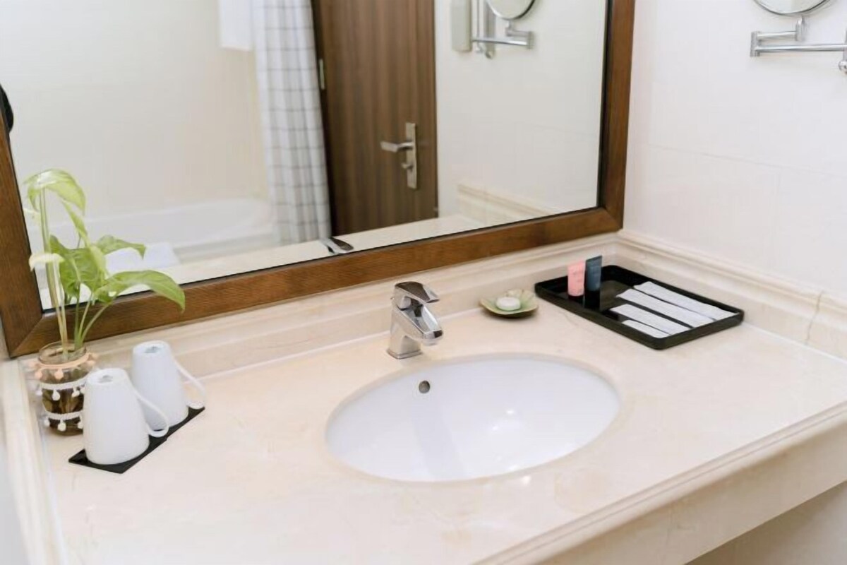 A bathroom with a sink, mirror, toiletries, and a plant.