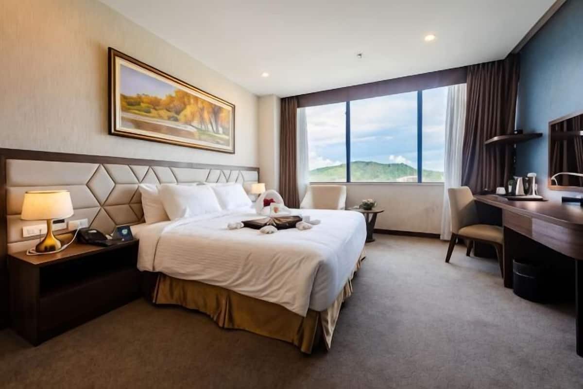 A hotel room with a bed, bedside tables, a desk, a chair, and a large window.