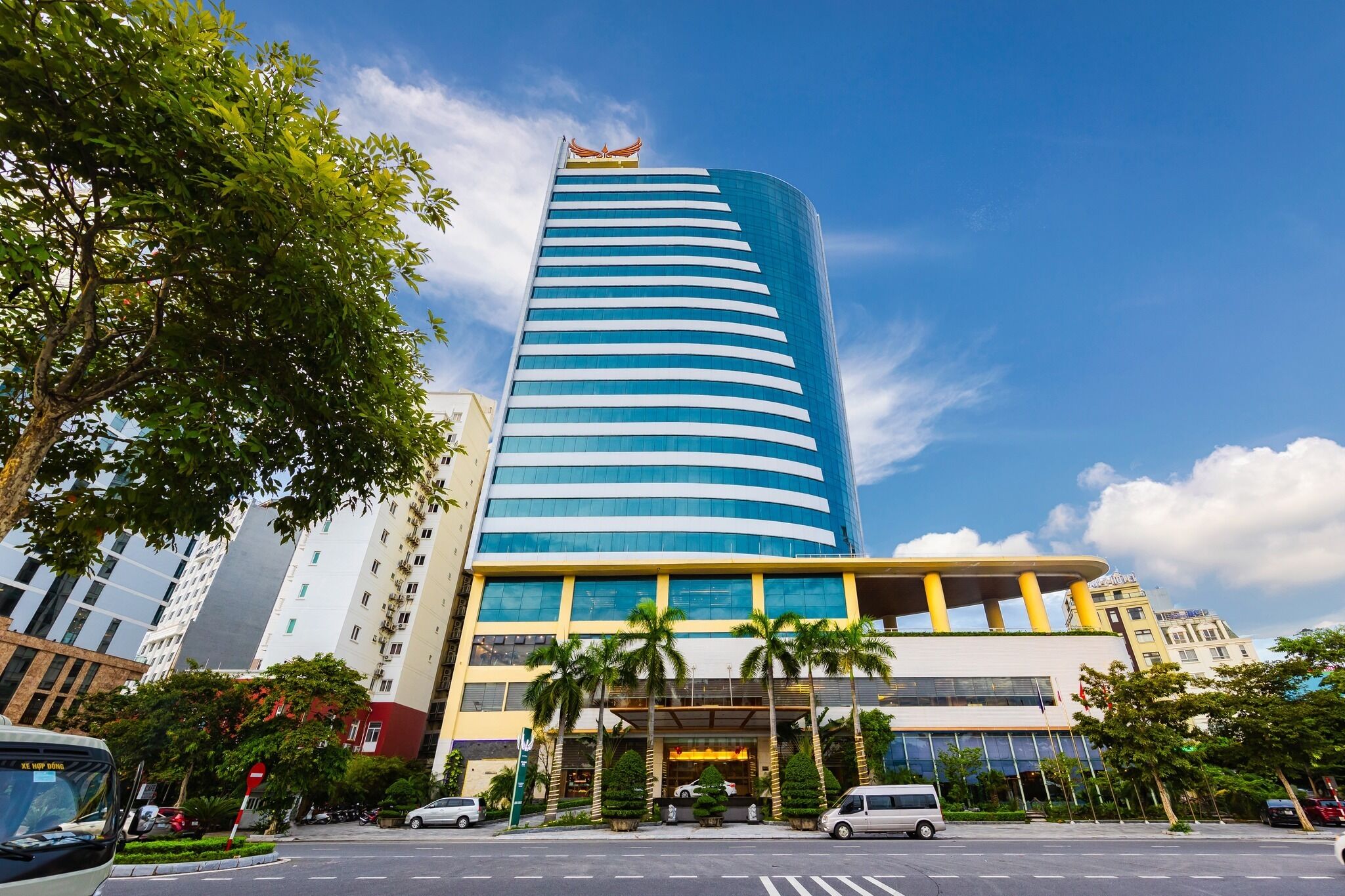 A modern hotel with a curved facade, multiple floors, and a prominent entrance with palm trees.