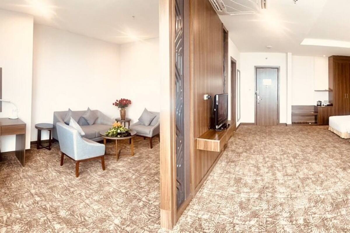 A hotel room with a sofa, two armchairs, a coffee table, a TV, two beds, and a desk.