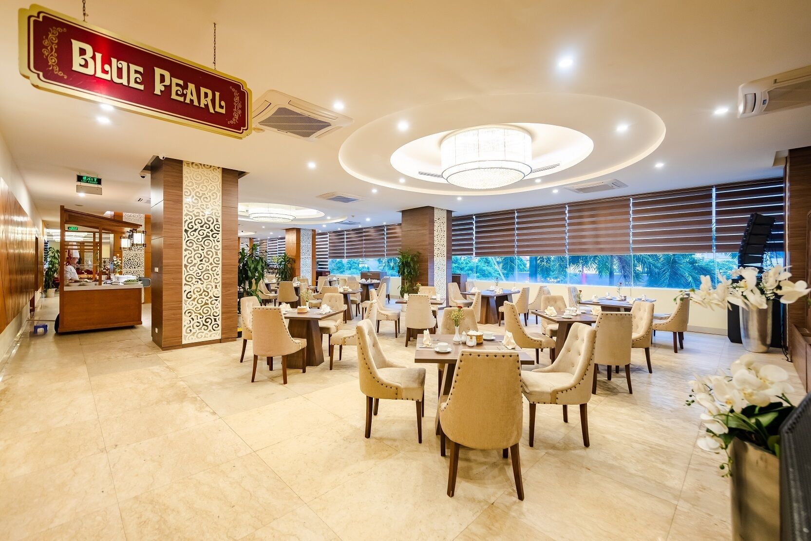 A spacious restaurant with multiple dining tables and chairs, a prominent sign reading "BLUE PEARL", and large windows offering a view of greenery outside.