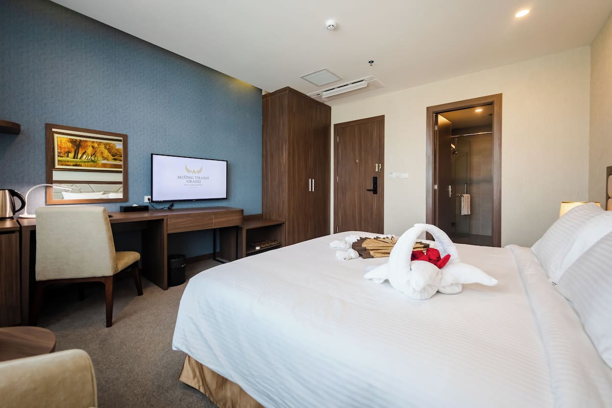 A hotel room with a bed, a desk, a chair, a TV, and a wardrobe.