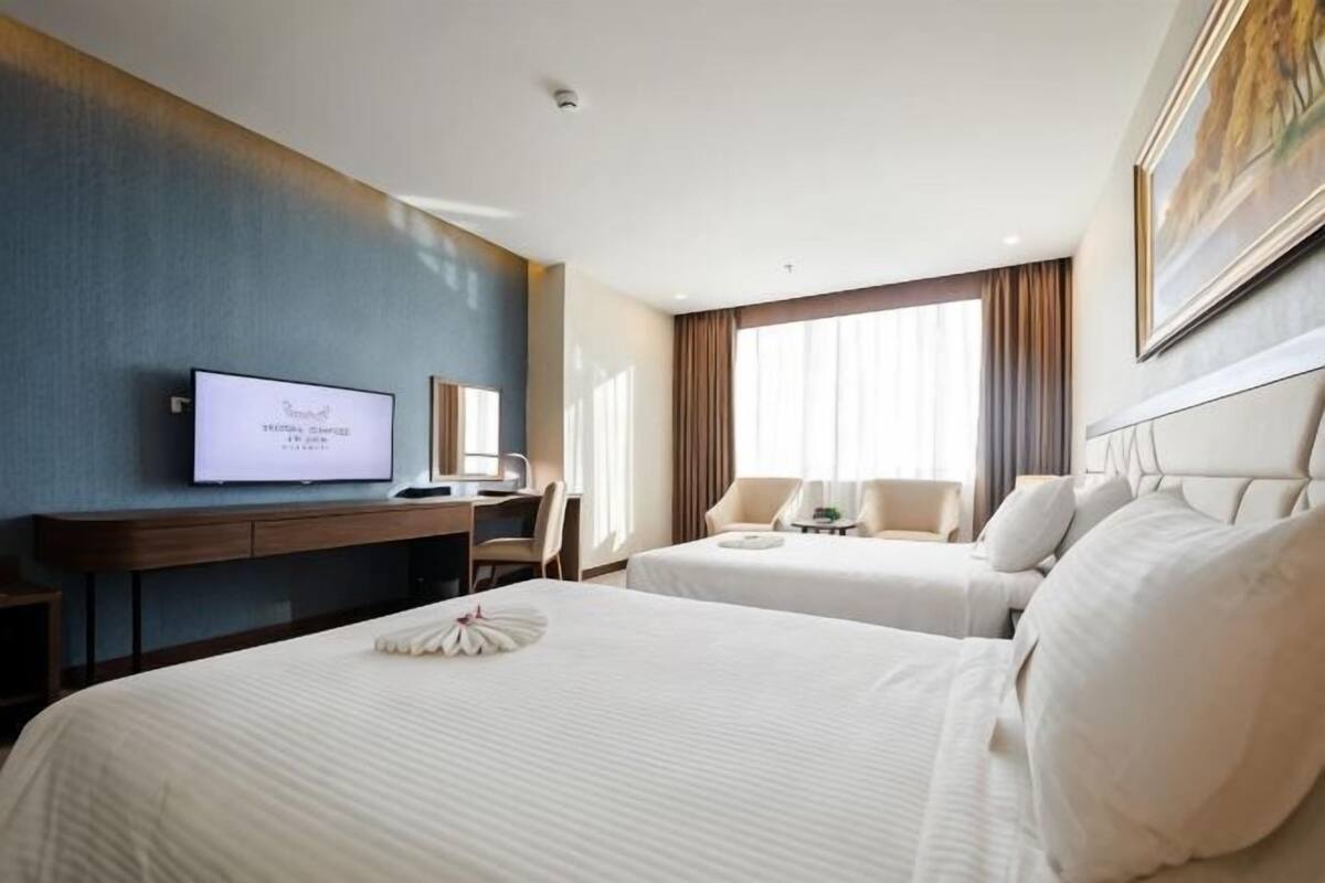 A hotel room with two beds, a desk with a computer, a television, and a large window with curtains.