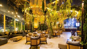 A well-lit indoor space with seating arrangements, including sofas and chairs, surrounded by greenery and hanging light fixtures. - Muong Thanh Grand Ha Long Hotel (Bai Chay)