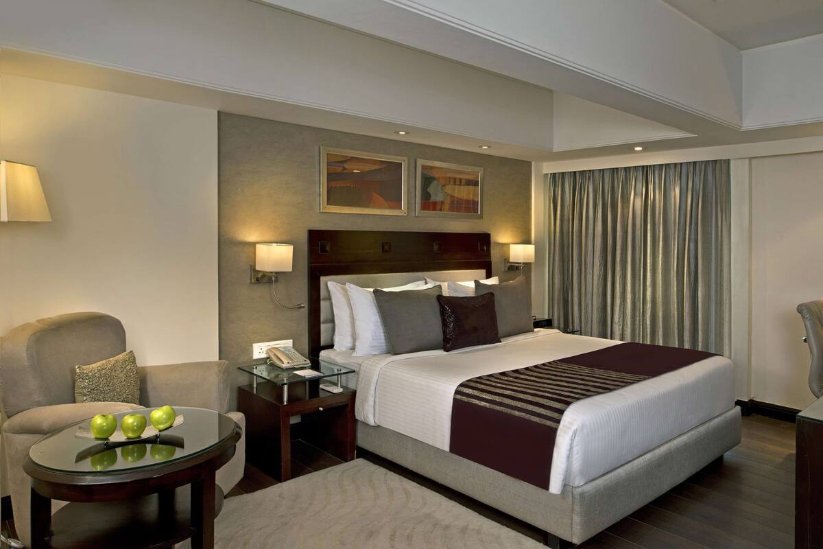 Una habitación de hotel con una cama grande, un escritorio con teléfono, una silla y una mesita con manzanas.