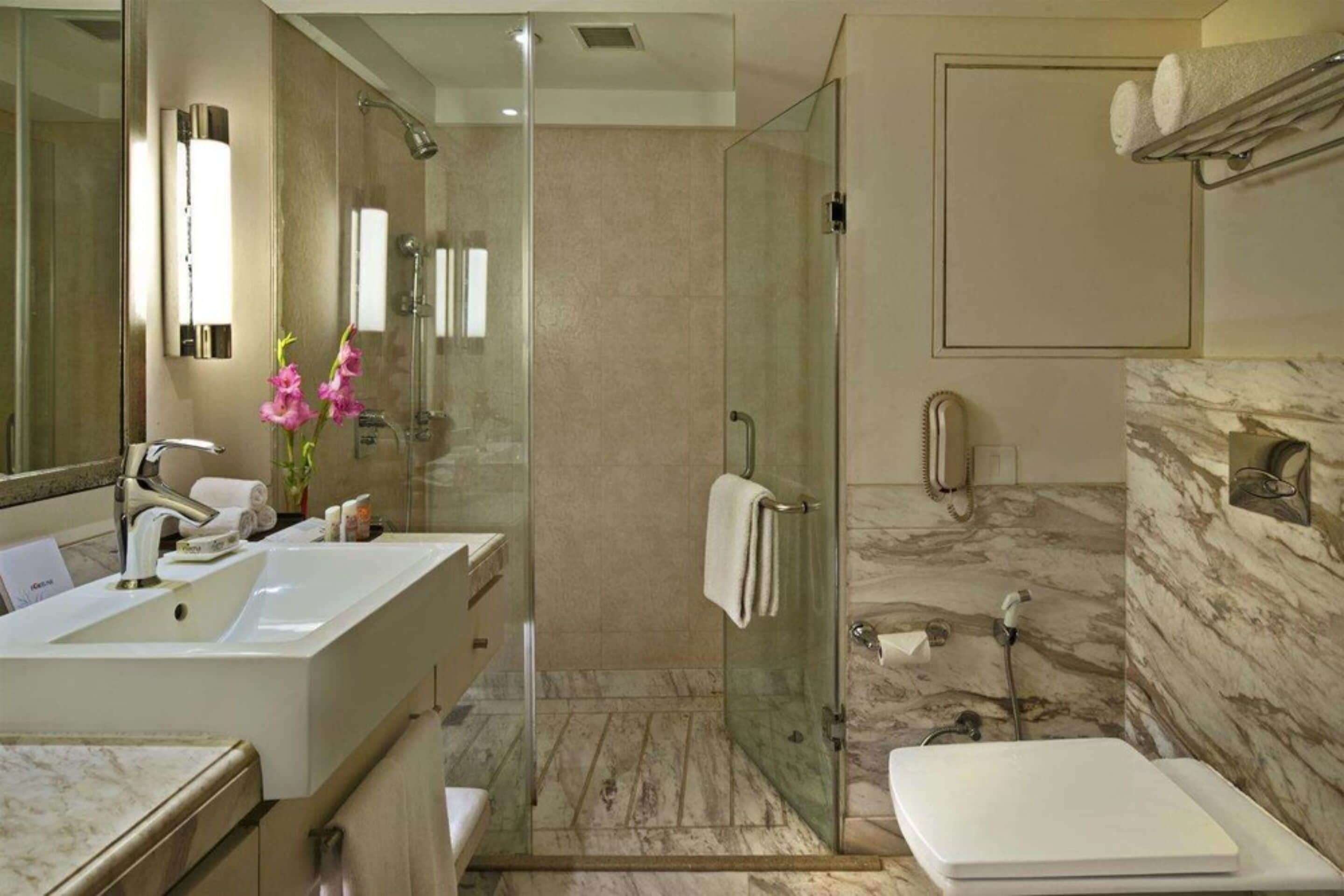 A modern bathroom with a glass-enclosed shower, a large sink, and a marble-tiled floor.