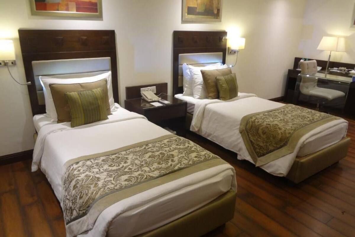Habitación de hotel con dos camas, cada una con cabecero, mesitas de noche y lámparas.