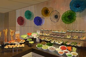 Un bufé con diferentes alimentos y coloridas decoraciones de vidrio en la pared.