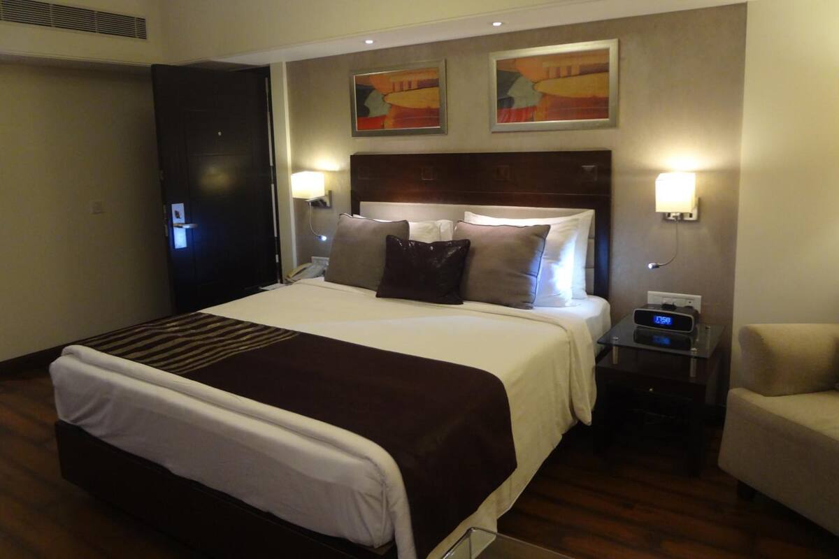Habitación de hotel con una cama grande, dos mesitas de noche, una silla y obras de arte en las paredes.