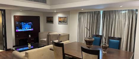 A modern dining area with a wooden table, upholstered chairs, a television, and artwork on the walls.