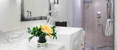 Un baño moderno con tocador de mármol, un espejo grande, un florero y una ducha a pie.
