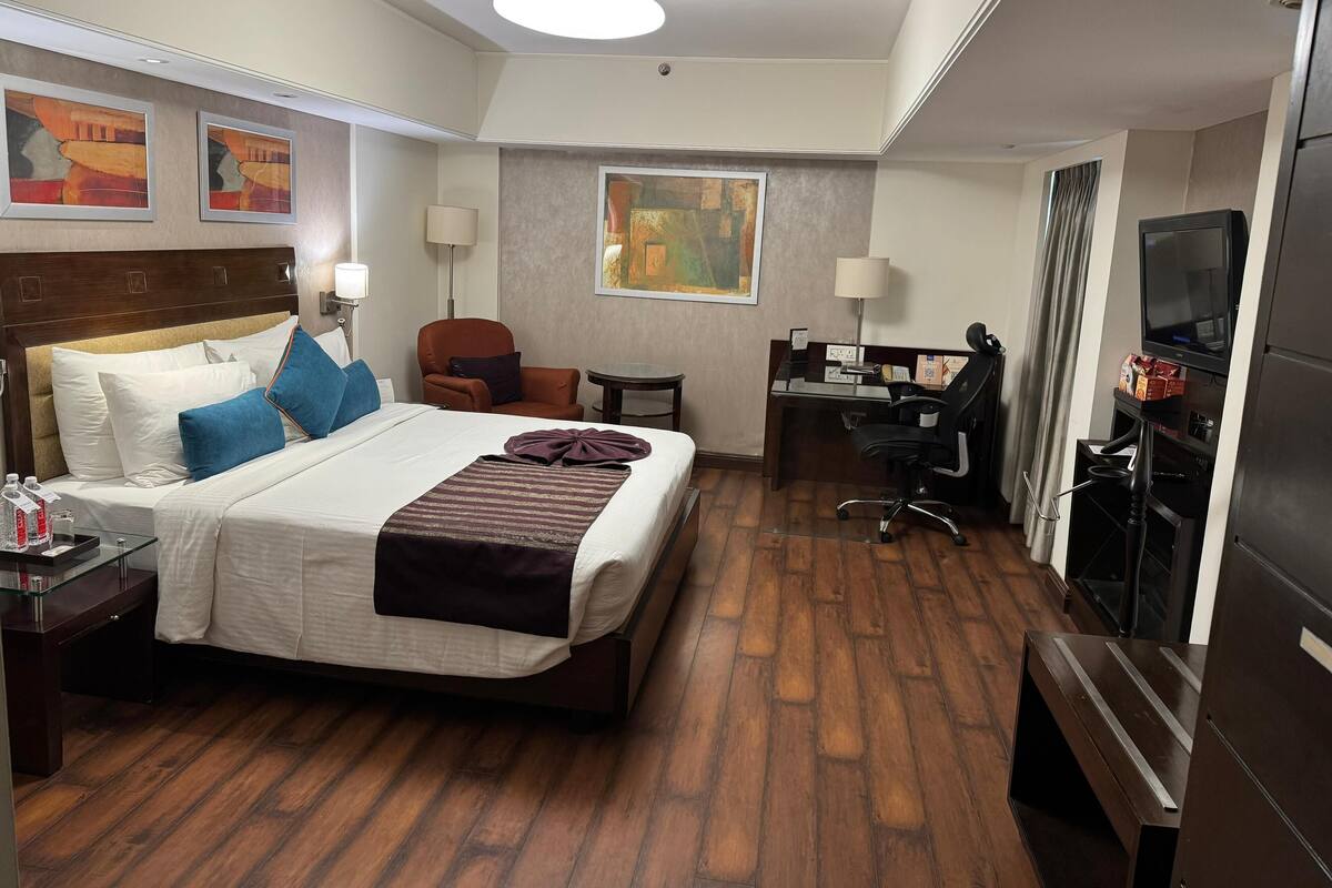 Una habitación de hotel con cama, escritorio, silla, televisor y un cuadro en la pared.
