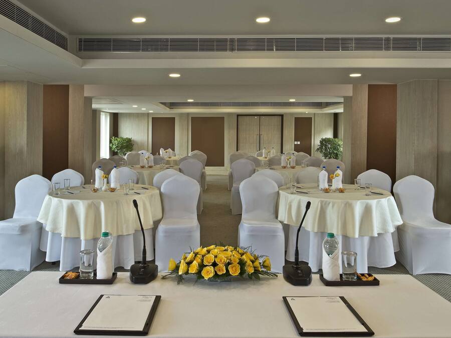 A conference room with round tables, white chairs, and a floral centerpiece.