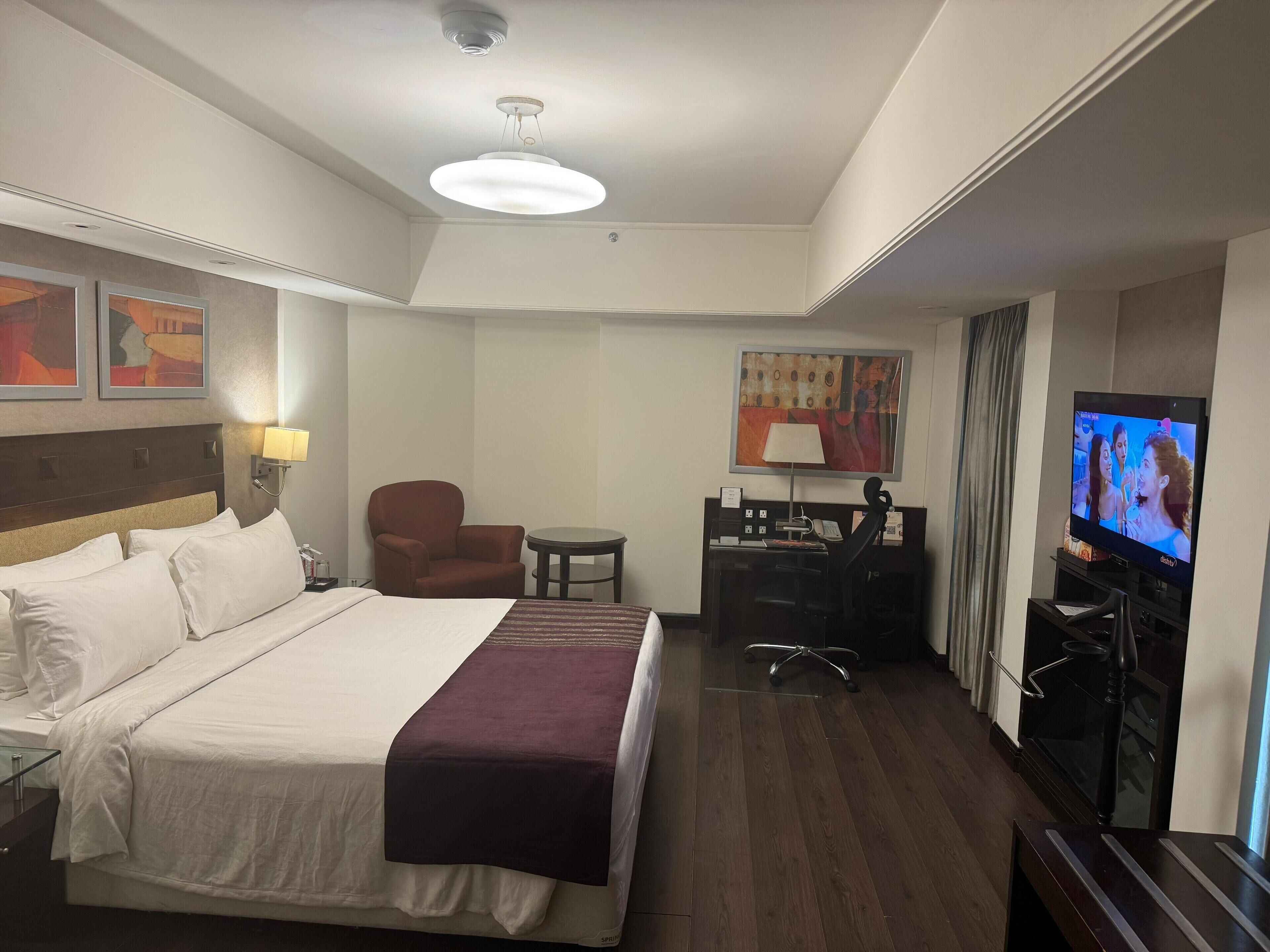 A hotel room with a bed, a desk with a chair, a television, and artwork on the walls.