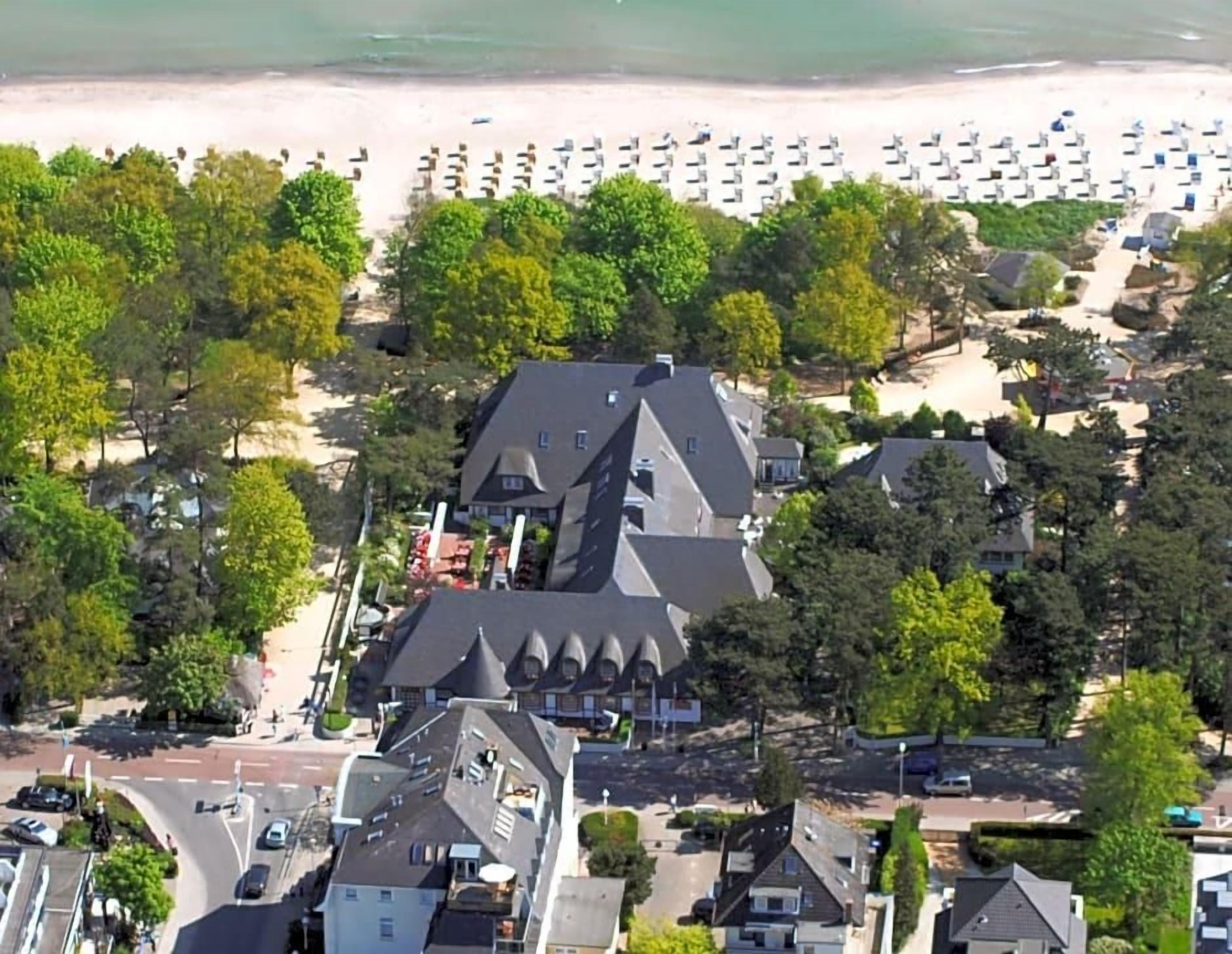 Luftaufnahme einer Küstenlandschaft mit Strand, geparkten Autos und Gebäuden mit markanter Architektur.
