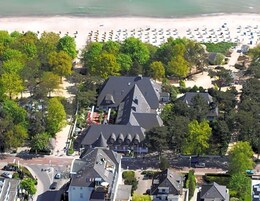 Luftaufnahme einer Küstenlandschaft mit Strand, geparkten Autos und Gebäuden mit markanter Architektur.