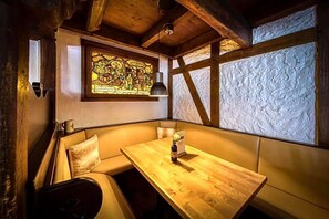 A cozy corner with a wooden table, cushioned seating, a stained glass window, and textured wall panels. - Carstens Landhaus (Timmendorfer Strand)