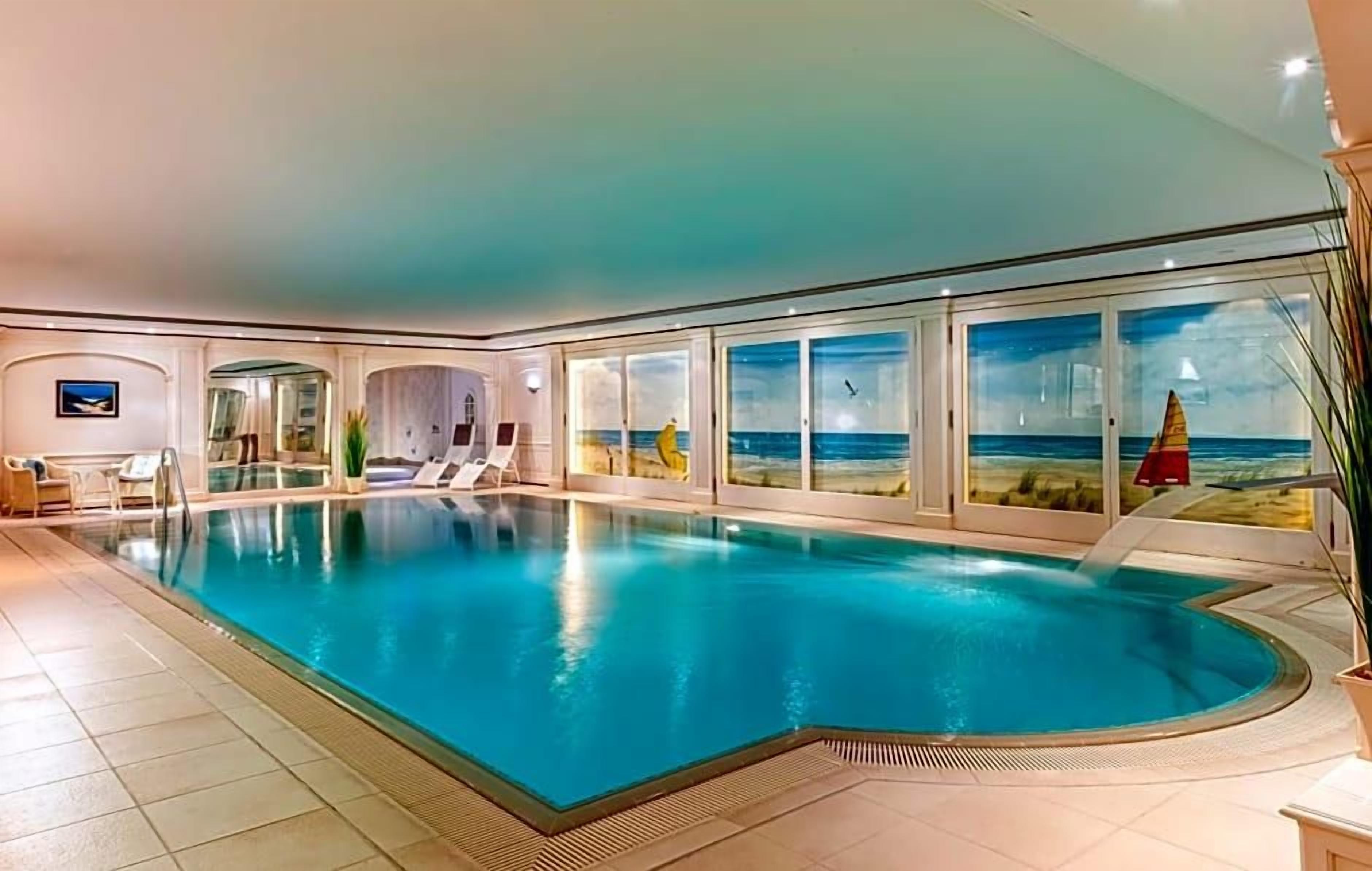 Ein großer, überdachter Schwimmbereich mit Glaswänden, einer Liege und Blick aufs Meer.
